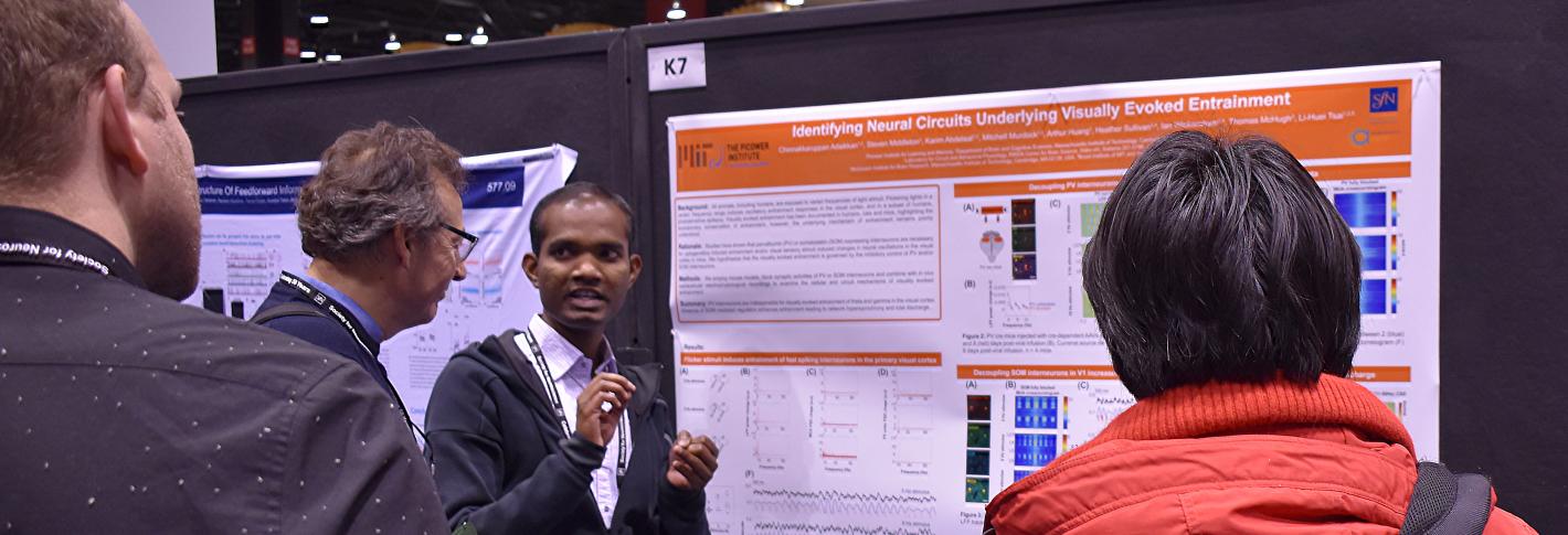 Chinna Adaikkan gestures as he stands at his research poster explaining it to three onlookers