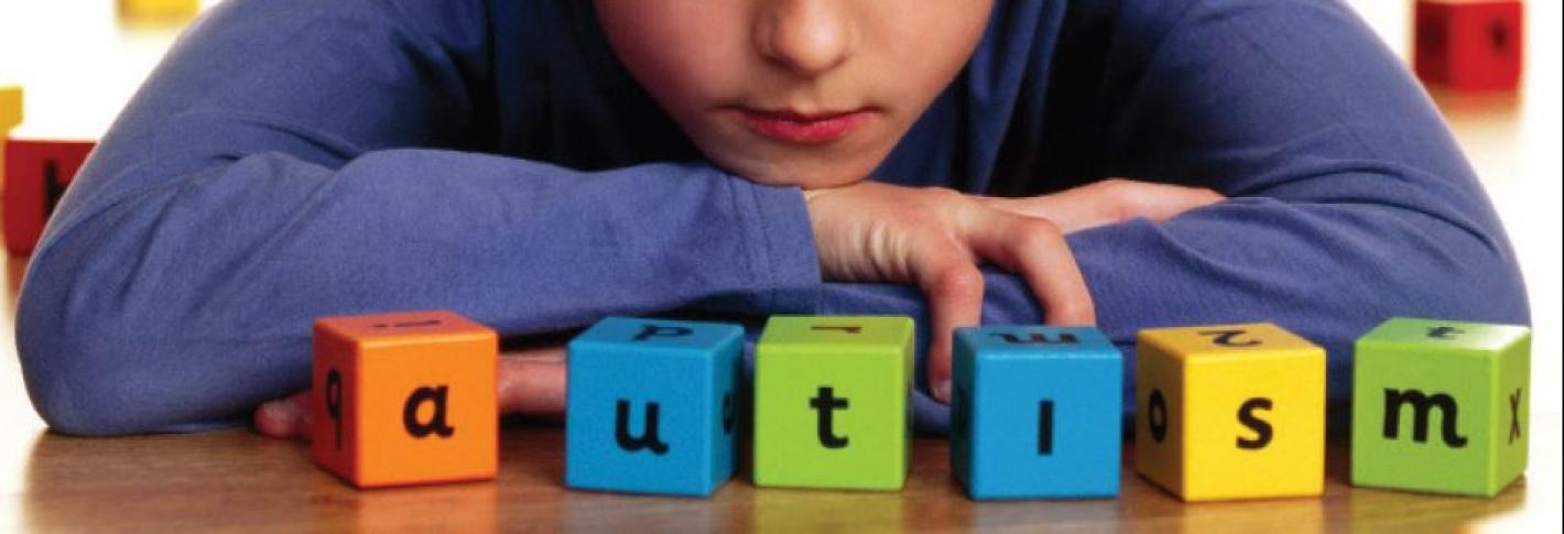 A boy sits with letter blocks that spell AUTISM