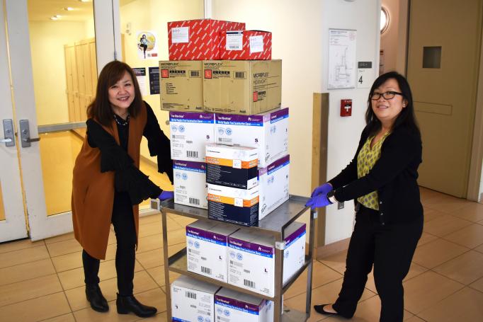 Two women push a rolling cart full of boxes of biomedical supplies