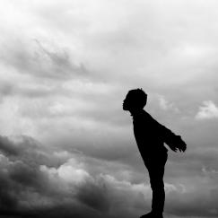 Silhouette of a child leaning toward a dark cloudmass, as if blowing the dark clouds away