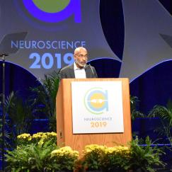 Emery Brown speaks at the SfN podium with flowers on the stage below