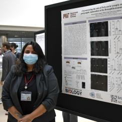 Patricia Pujols, wearing a surgical mask, stands next to her research poster in the Building 46 atrium