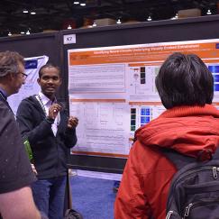 Chinna Adaikkan gestures as he stands at his research poster explaining it to three onlookers