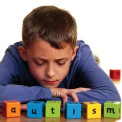 A boy sits with letter blocks that spell AUTISM