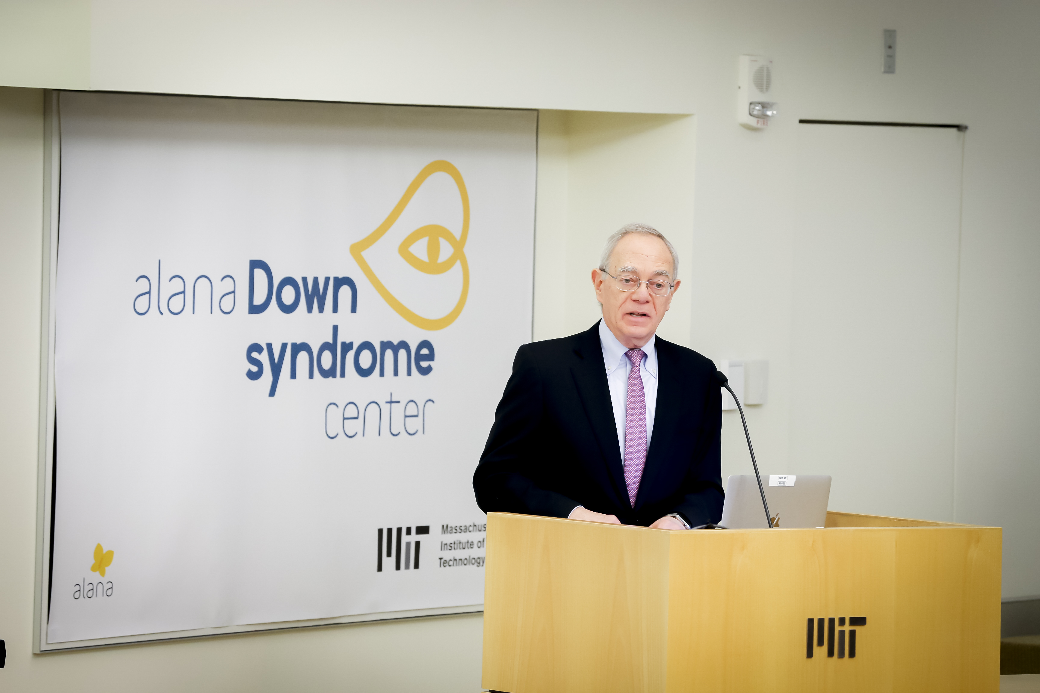 Rafael Reif stands at a lectern with a sign behind him reading Alana Down Syndrome Center