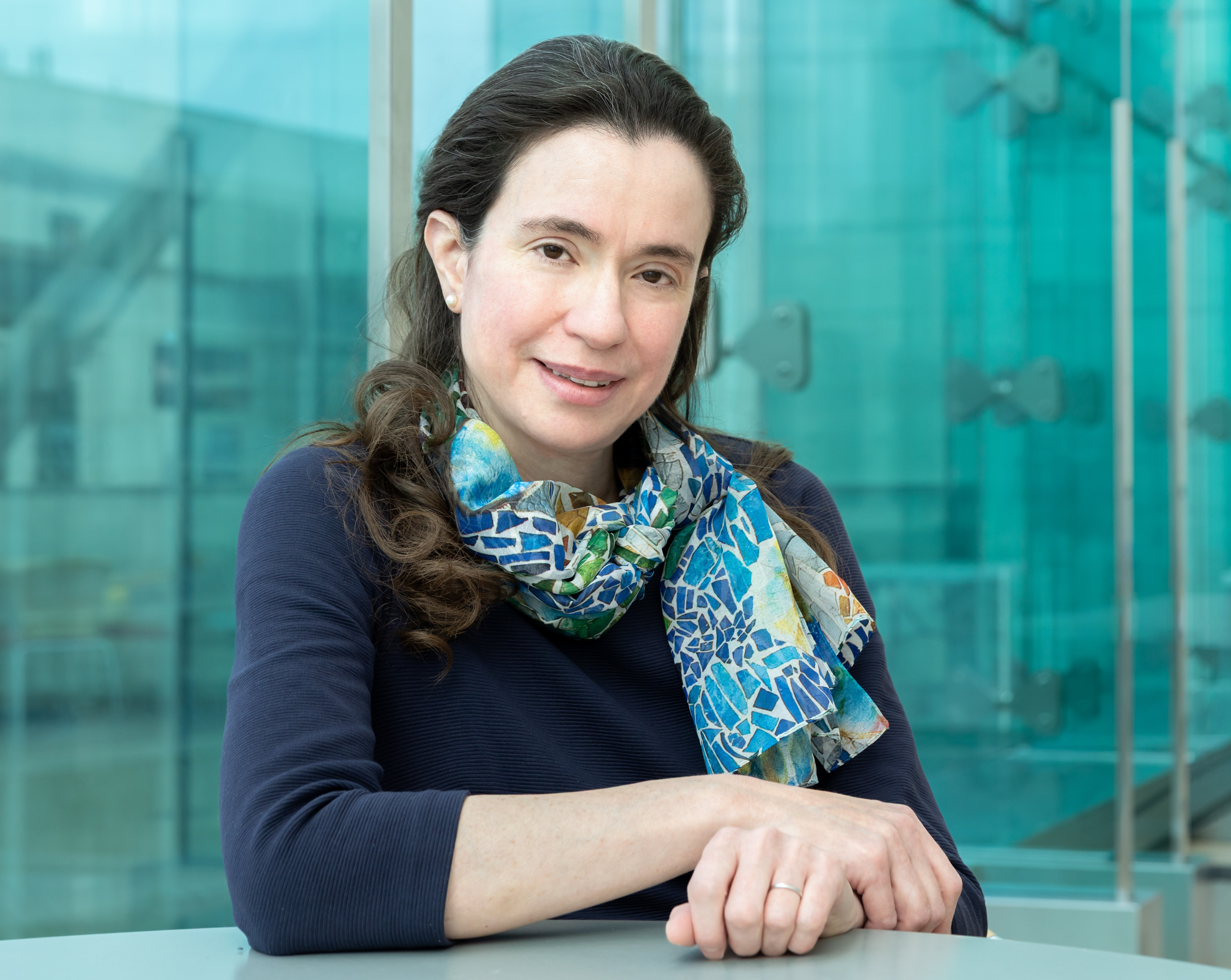 Myriam Heiman sits at a table in front of the blue glassy windows of the reading terrace in MIT's building 46