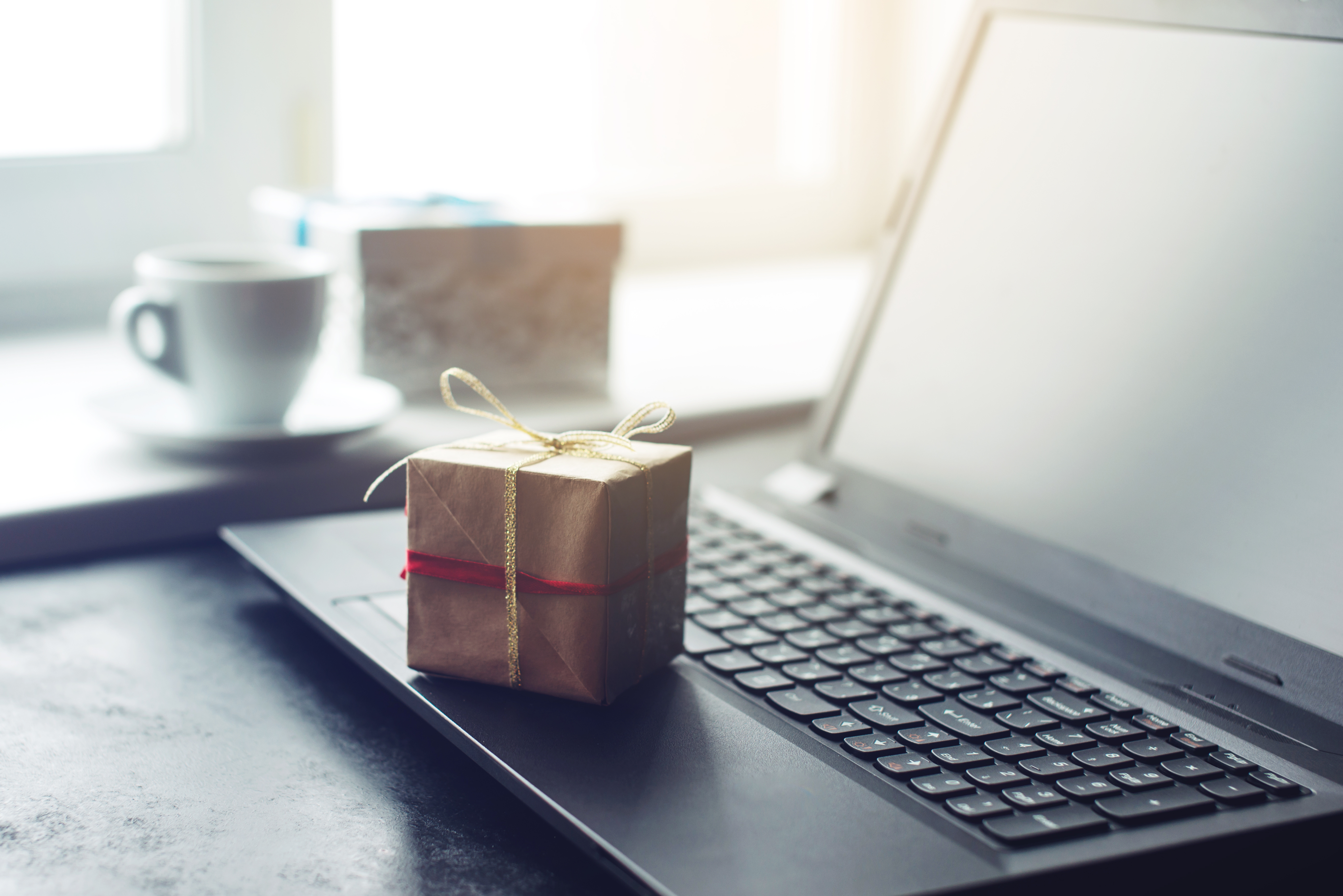 A small present wrrapped in brown paper and twine sits atop a laptop on a desk