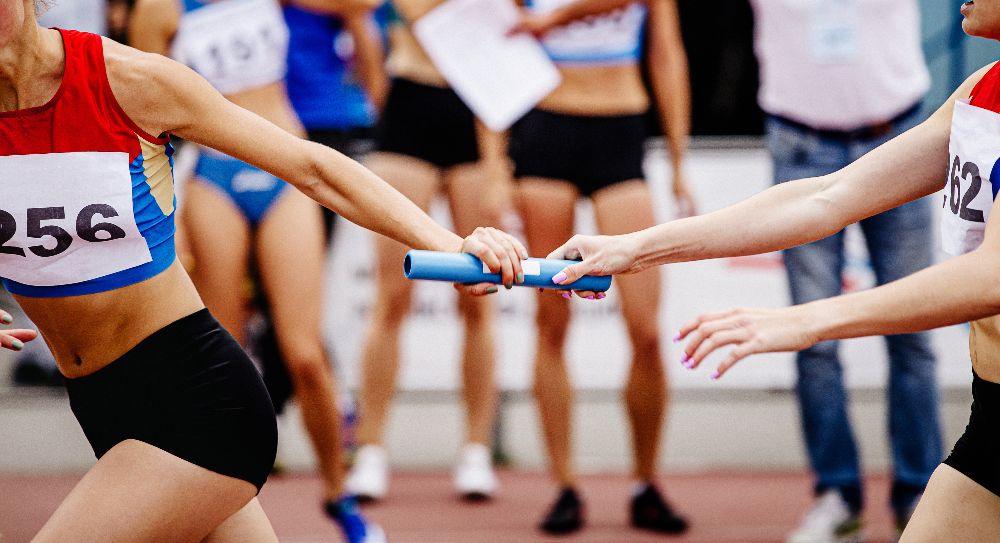 A closeup on two relay racers as they hand off a blue baton from one runner to the other.