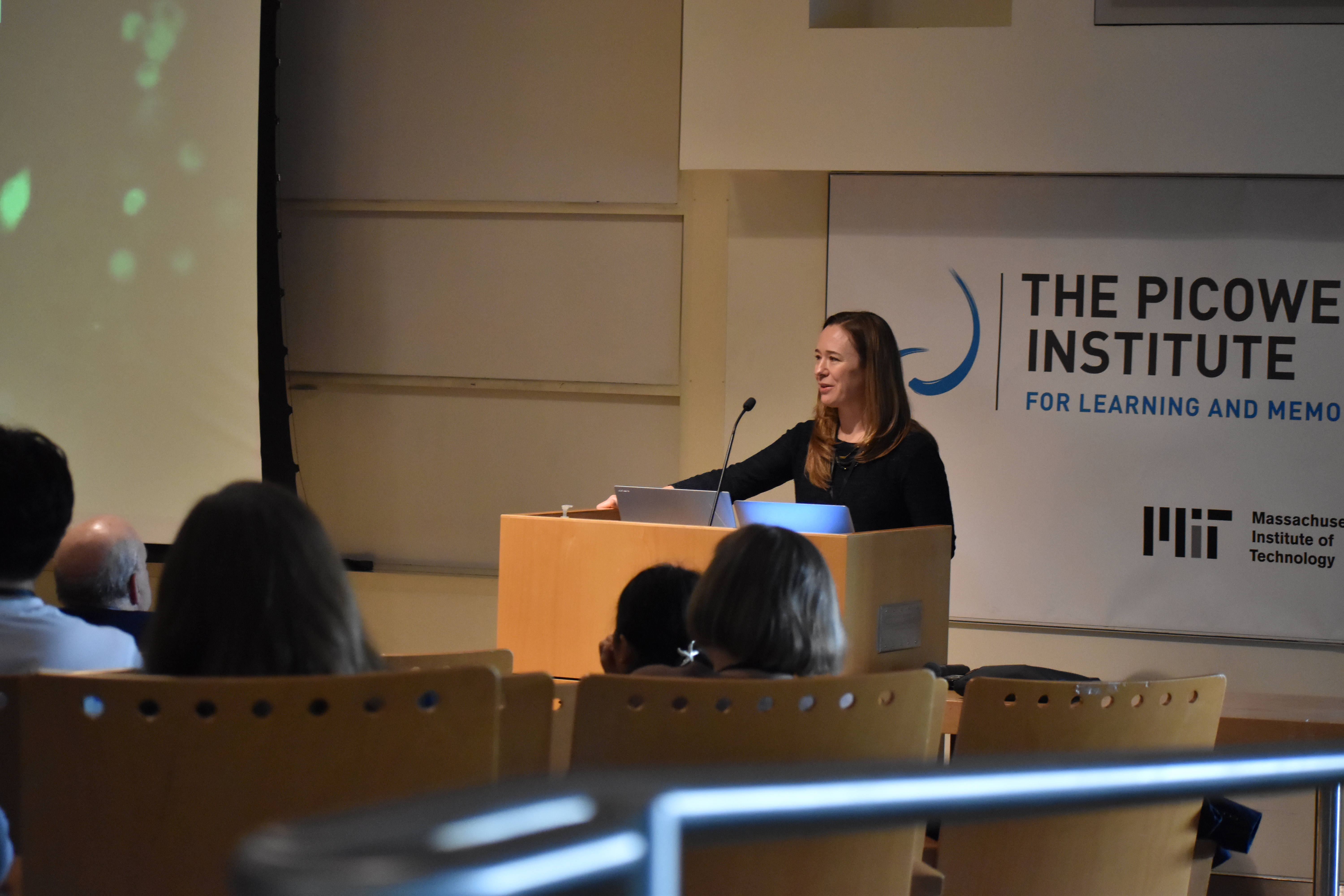 Sara Prescott stands at the podium in MIT's Singleton Auditorium speaking to an audience in the foreground