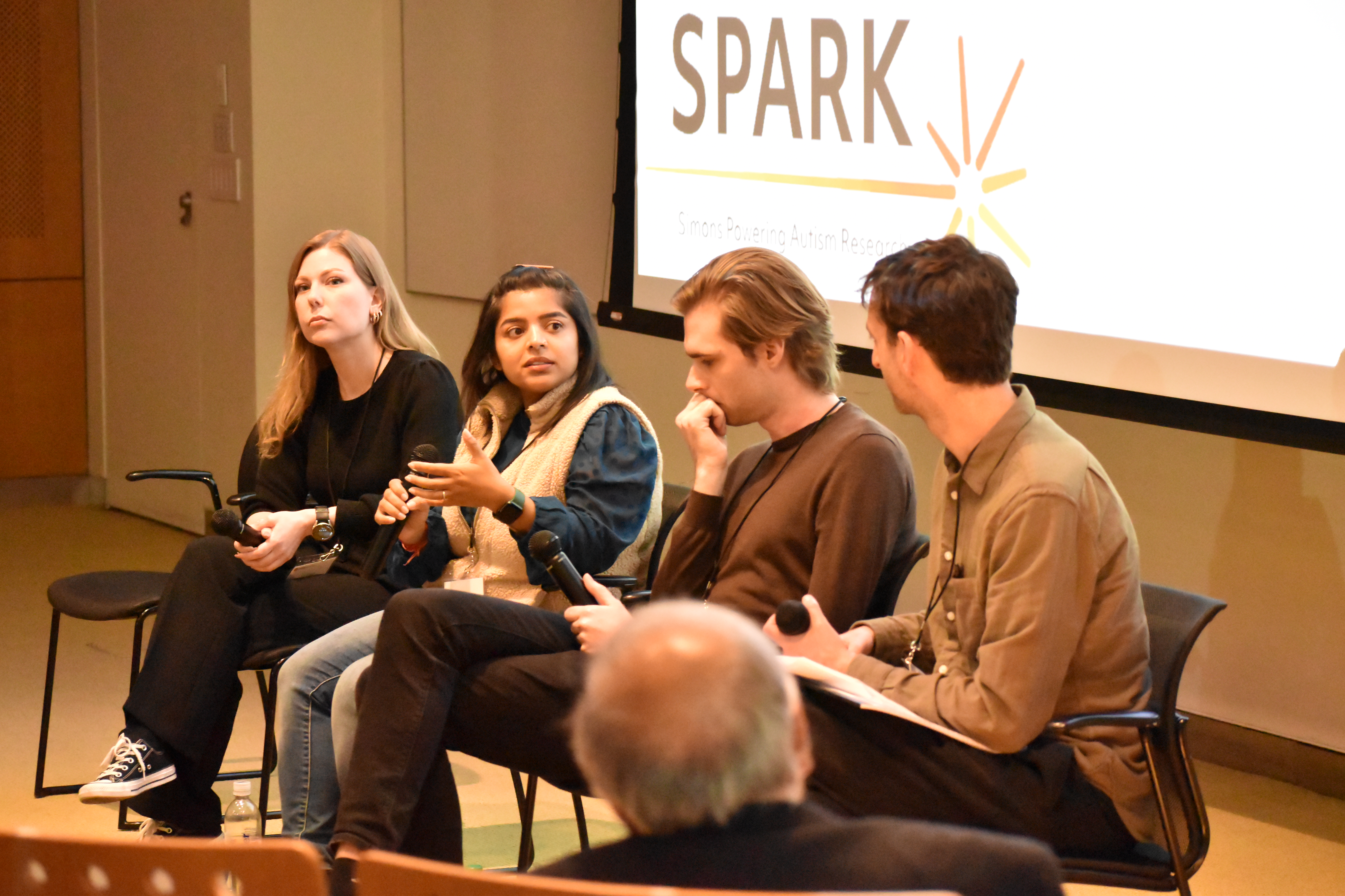 Lace Riggs, Chhavi Sood, Lukas Vogelsang and Michael Sege sit in chairs on a stage in front of a screen.