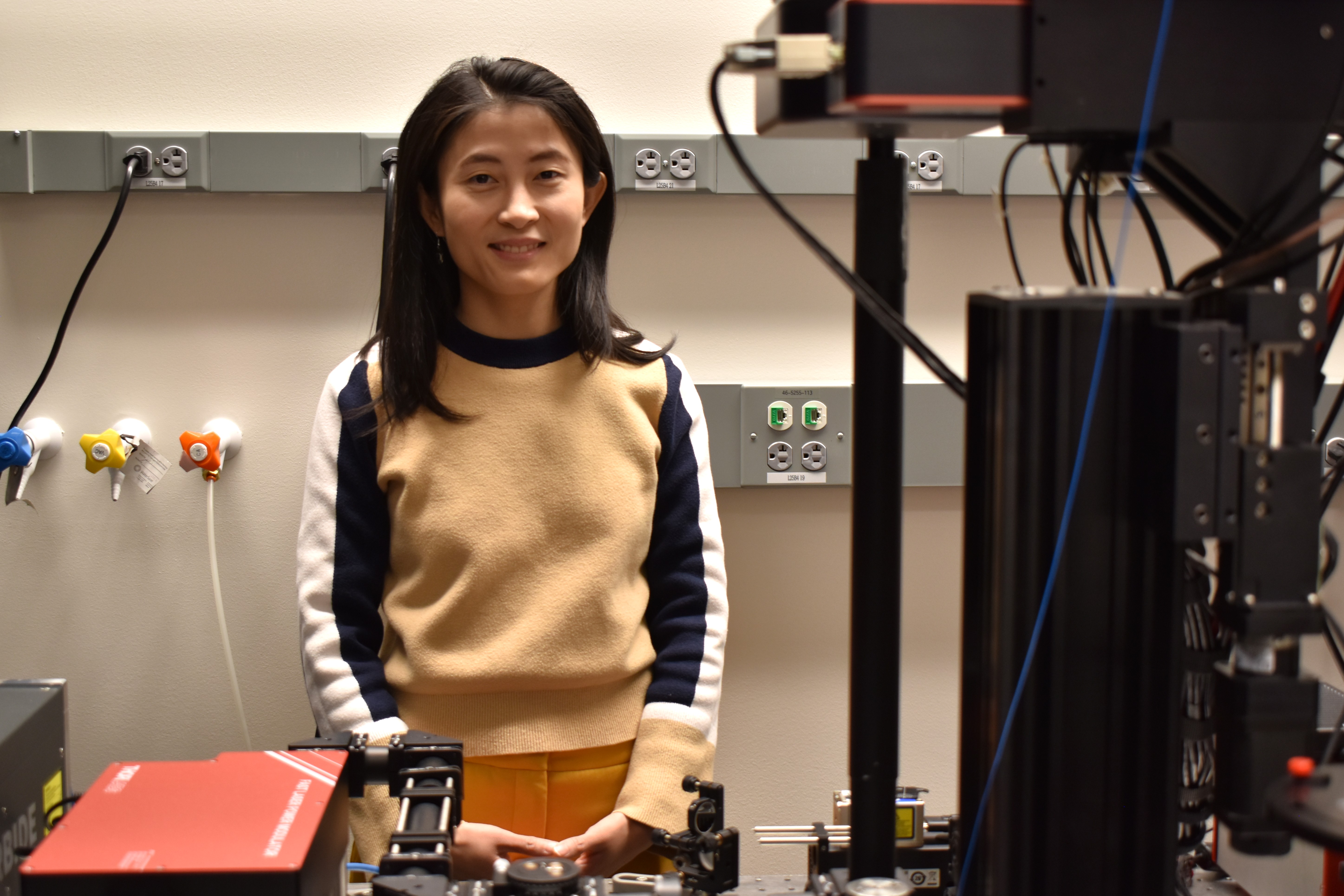 Linlin Fan stands in her lab with microscope equipment in the foreground.