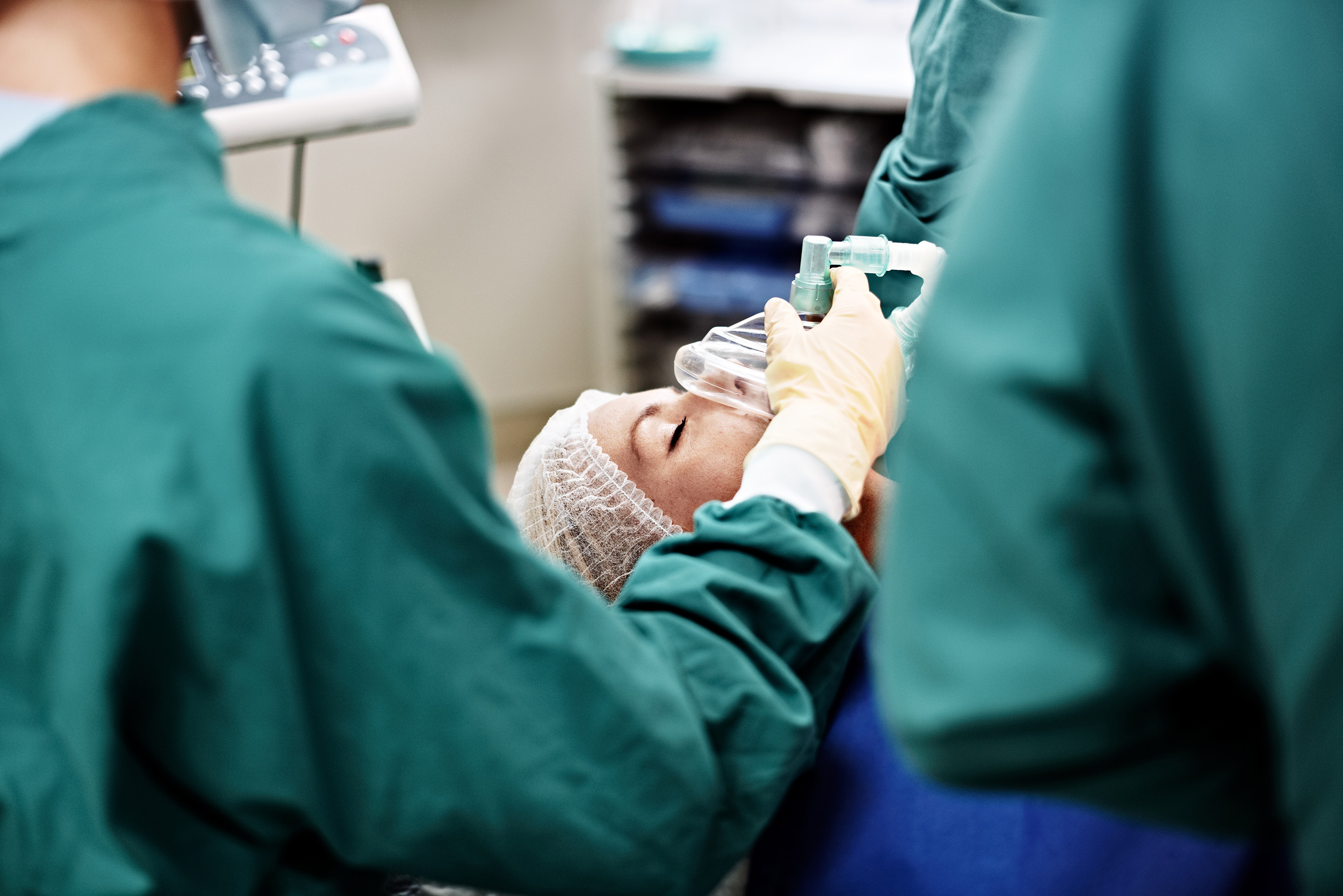 A member of a surgical staff holds a mask on the face of an unconscious patient in an operating room