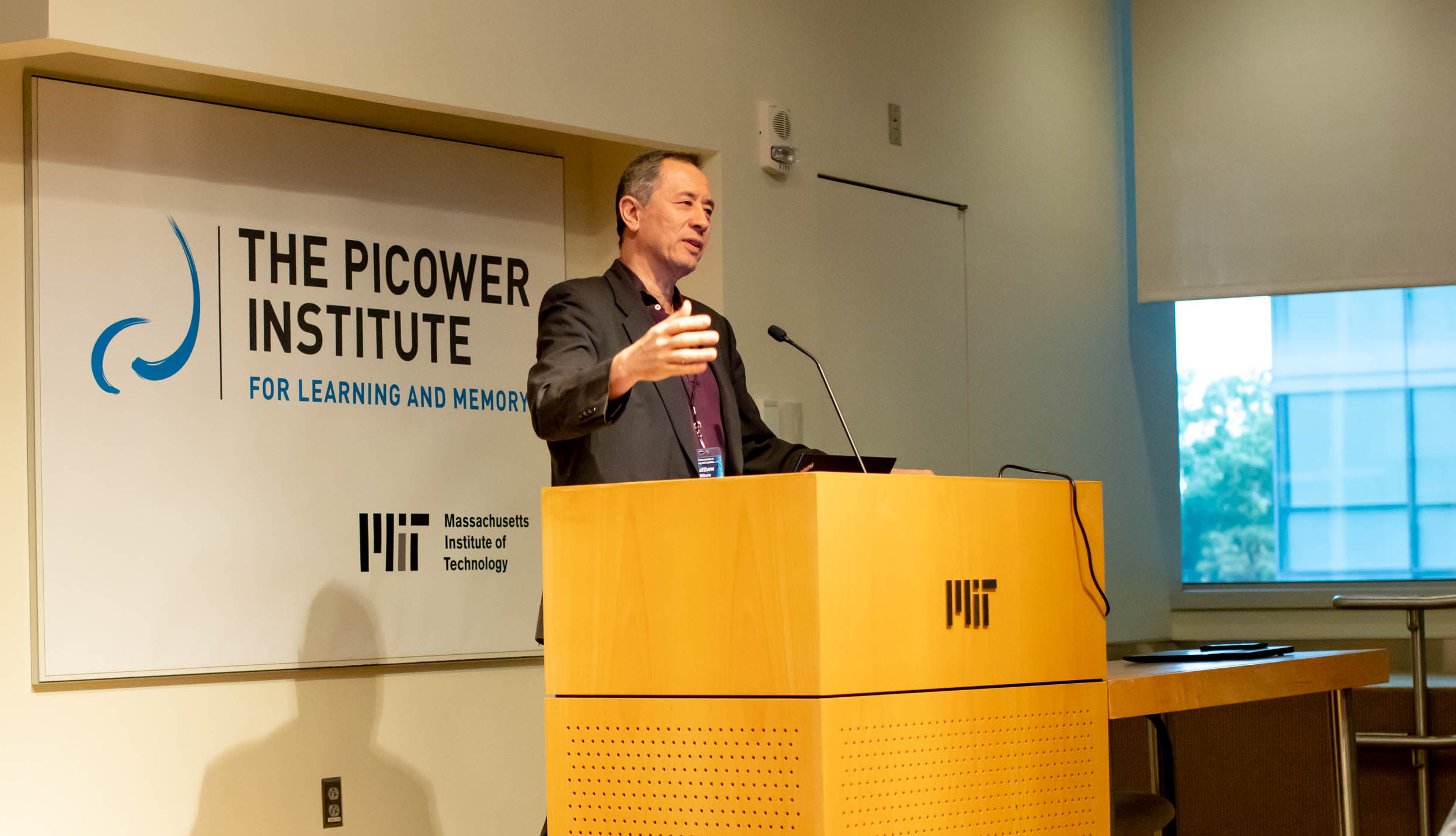 Matthew Wilson stands at an MIT podium with the Picower Institute logo behind him