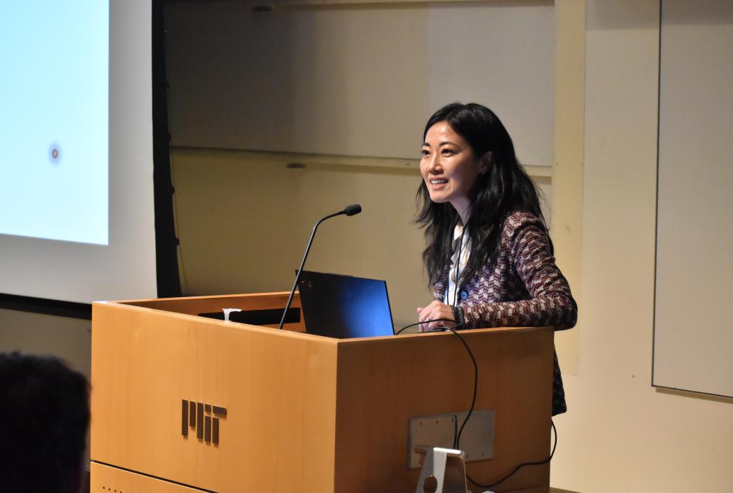 Gloria Choi stands at a wooden lectern with an MIT sign on it.