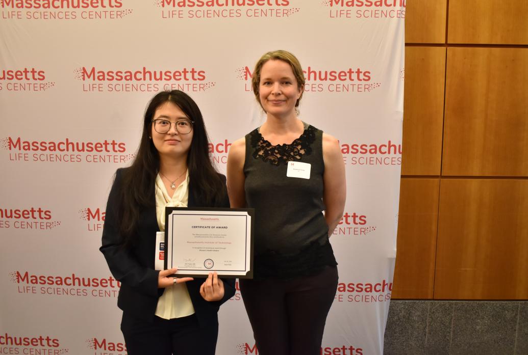 Shanshan Zhang and Rosie Firenze stand before a Massachusetts Life Sciences Center backdrop holding and award certificate