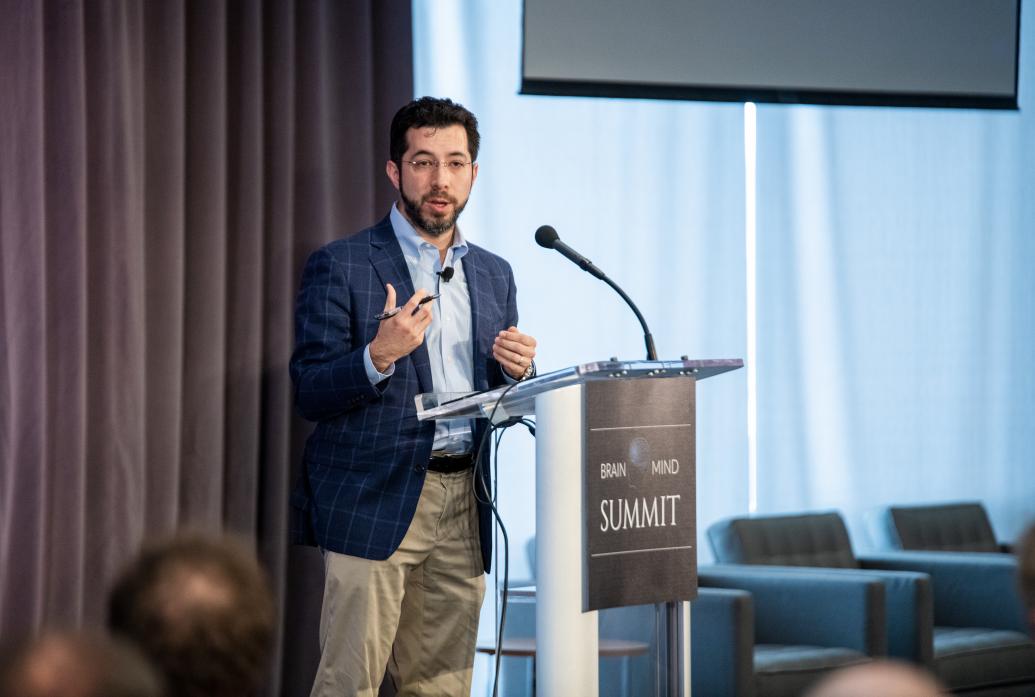 Ed Boyden stands and gestures at the podium of the Brain Mind Summit