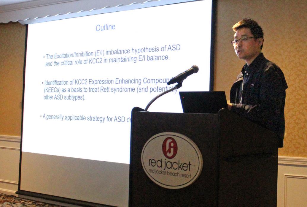 Xin Tang speaks at a lectern with his talk outline on the screen behind him