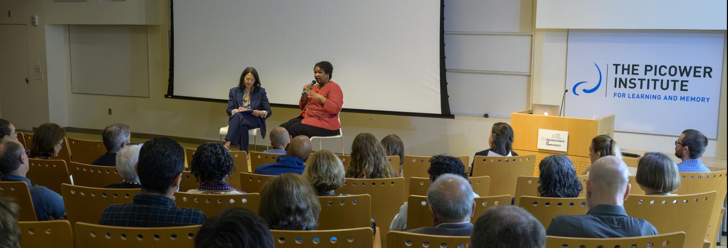 A view from behind the audience in Singleton Auditorium as Stacey Abrams and Felicia Wong sit in chairs on the stage and talk.