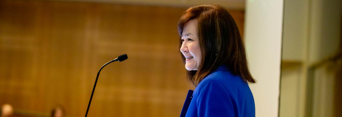 Li-Huei Tsai smiles in a profile view as she stands at a lectern