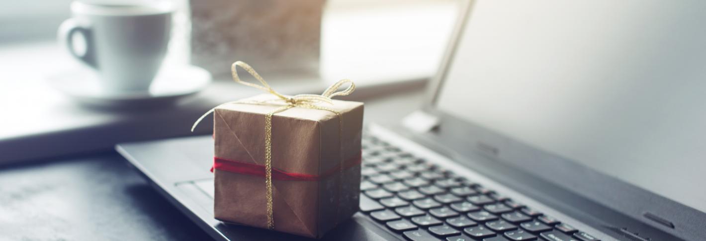 A small present wrrapped in brown paper and twine sits atop a laptop on a desk