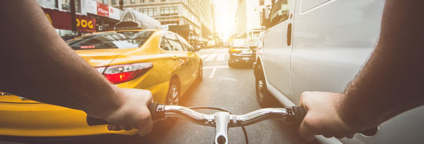 A point of view of a cyclist on a busy manhattan street with a van an taxi alongside the bike