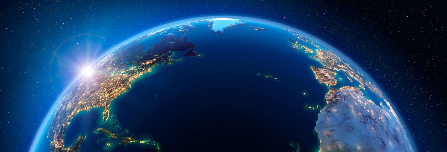 A satellie view of the world centerd on the Atlantic Ocean. The sun is setting over the Pacific Northwest and lights are on across the Americas and Europe and West Africa.