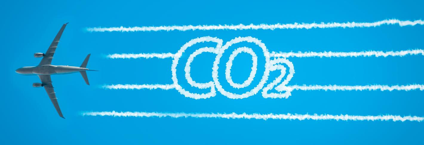 An airplaine seen from below extends contrails that take the form of the letters CO2