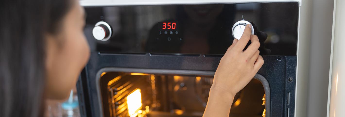 A woman turns a dial on an oven with cookies inside. The oven's display shows 350 indicating the temperature setting she has chosen.