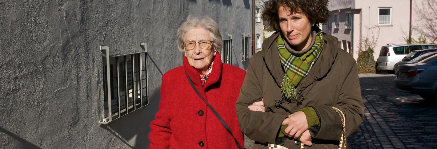 An old woman holds the arm of a younger one as they walk down the street