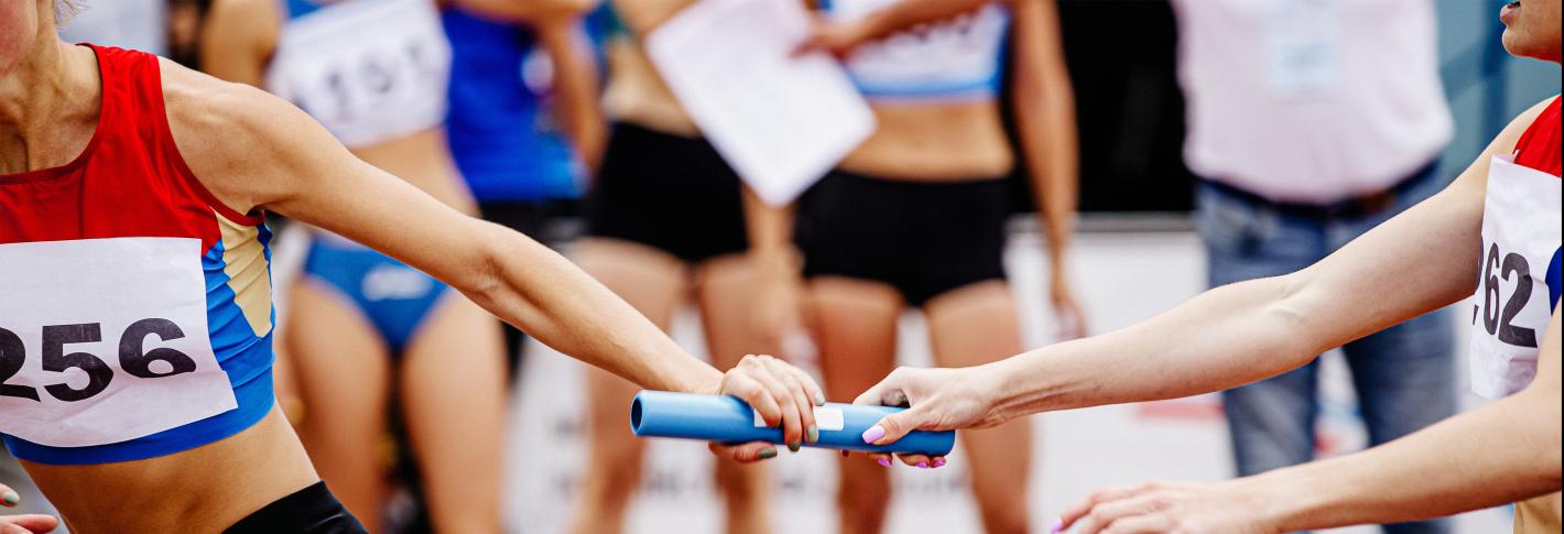 A closeup on two relay racers as they hand off a blue baton from one runner to the other.