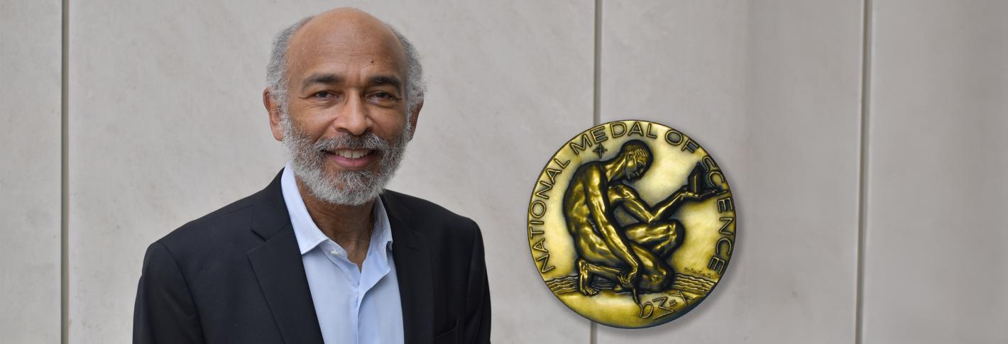 Emery N. Brown stands in front of a wall. Superimposed on the image next to him is a picture of the front of the National Medal of Science, which depicts a man kneeling and drawing an abstract character in the ground next to him as he contemplates an object.