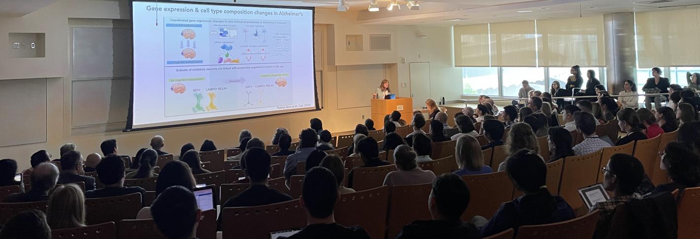 A packed auditorium looks on as Li-Huei Tsai presents a slide