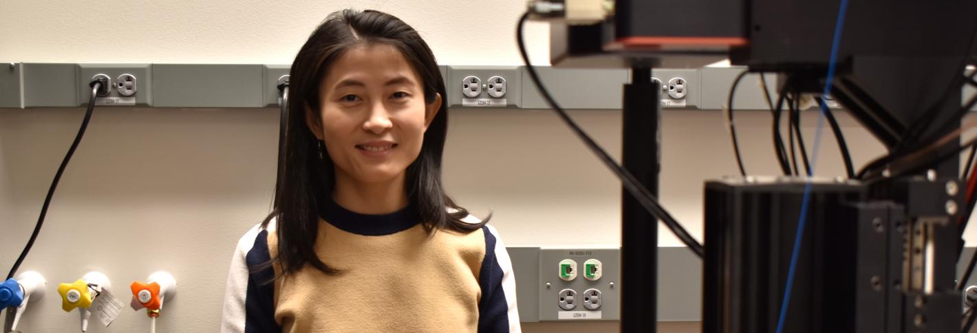 Linlin Fan stands in her lab with microscope equipment in the foreground.