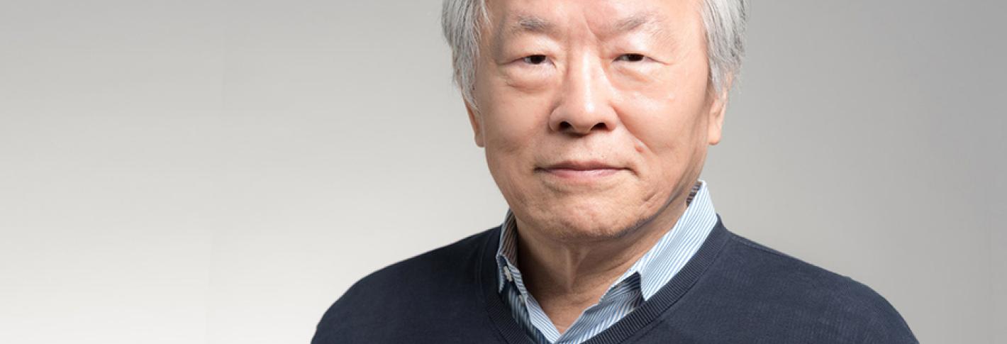 A portrait of Susumu Tonegawa in front of a gray background