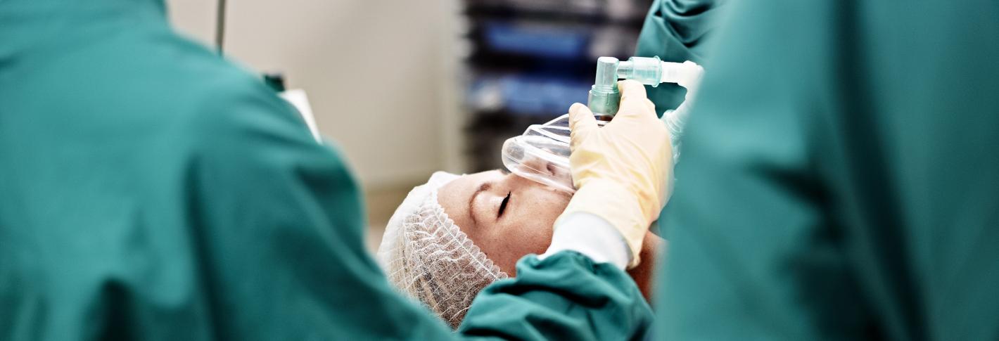 A member of a surgical staff holds a mask on the face of an unconscious patient in an operating room