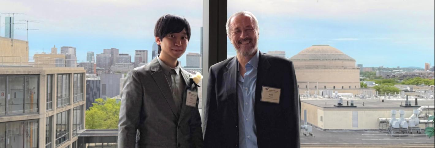 Takato Honda and Matt Wilson stand side by side and smile in front of a window overlooking other campus buildings including the Great Dome.