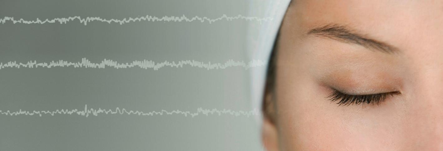 A closeup on the right half of a sleeping woman's face is flanked on her right (our left) with white brainwaves extending across the image over a grey background