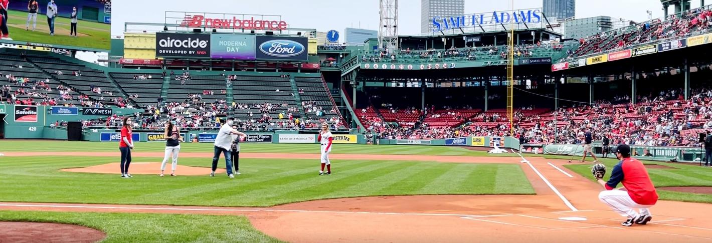 A view from the third base line at Fenway shows five people standing near the mound. One has thrown a ball that's on the way to the catcher.