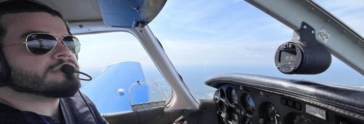 Francis Reilly-Andujar looks out through the windows of the cockpit of a plain while he holds the yoke.