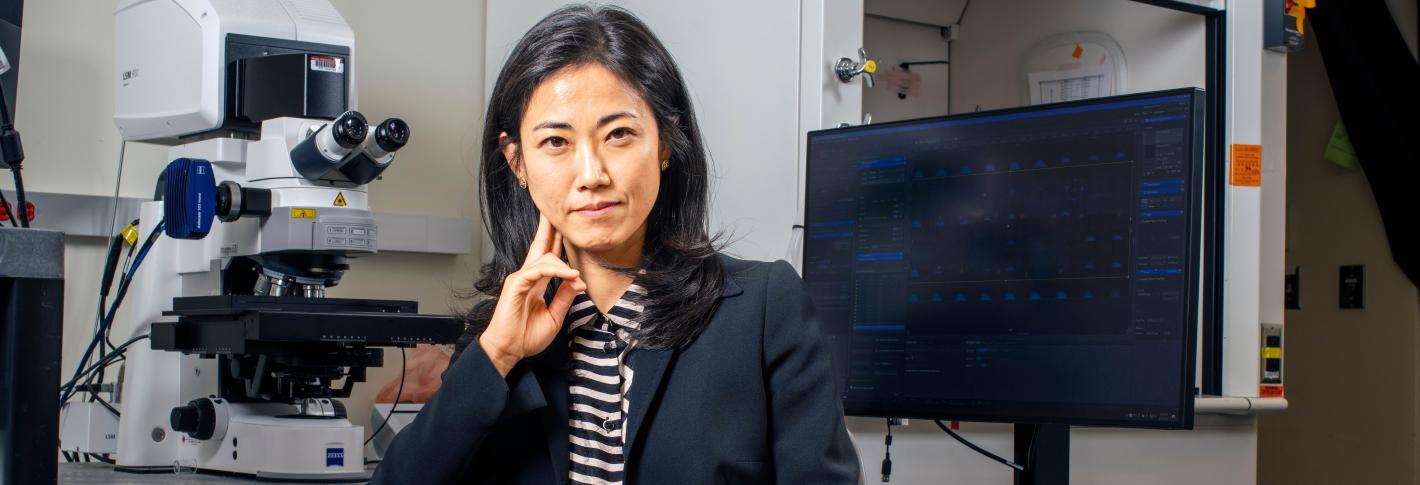 Gloria Choi looks directly at the camera as she sits at a microscope station in her lab