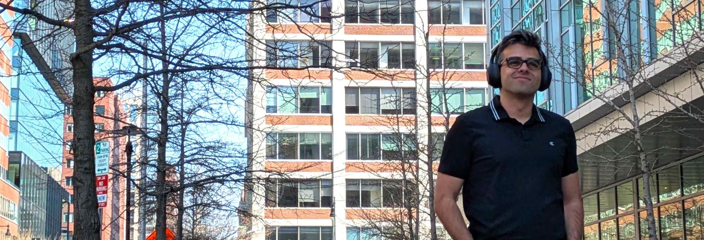 Ignacio (Nacho) Castillejo walks down a city street and smiles as he wears his over the ear headphones