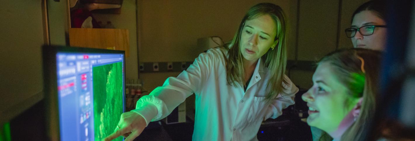 Sara Prescott points to a scientific image on a monitor in a lab as two students look on.