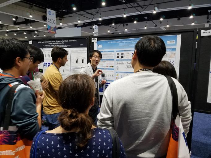 Chen Sun, in mid gesture, explains his research to several people surrounding him at his poster
