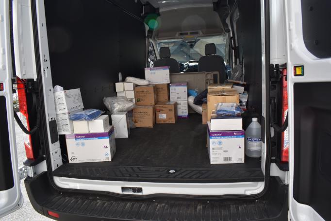 Boxes of supplies are loaded into the back of a large white van