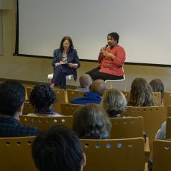 A view from behind the audience in Singleton Auditorium as Stacey Abrams and Felicia Wong sit in chairs on the stage and talk.