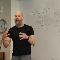 Earl K. Miller gestures as he talks while standing before a whiteboard where he has written several concepts including "cytoelectric coupling"