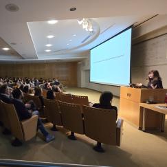 Li-Huei Tsai speaks at a podium in the front of MIT's Singleton auditorium, which full of audience members listening to her talk