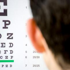 The viewer is situated behind the head of someone looking at an eye chart made up of increasingly small letters.