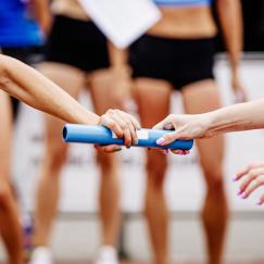 A closeup on two relay racers as they hand off a blue baton from one runner to the other.