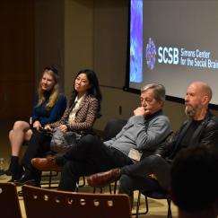 Ev Fedorenko, Gloria Choi, Charles Nelson and Earl Miller sit side by side on chairs in front of a screen displaying the logo of the Simons Center for the Social Brain.  Mriganka Sur stands nearby leaning on a podium and holding a microphone.